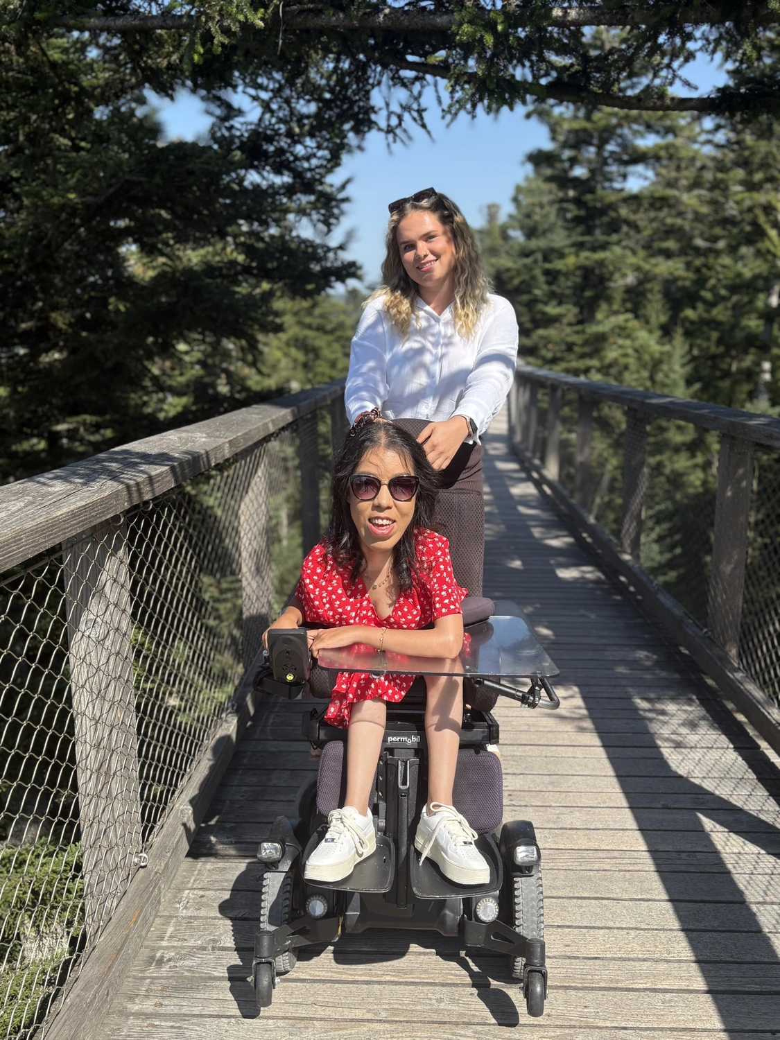 Hadzsi GbR - Assistenzdienstleistungen - Behinderte Frau sitzt in einem Elektrorollstuhl auf einer Brücke, begleitet von einer Frau